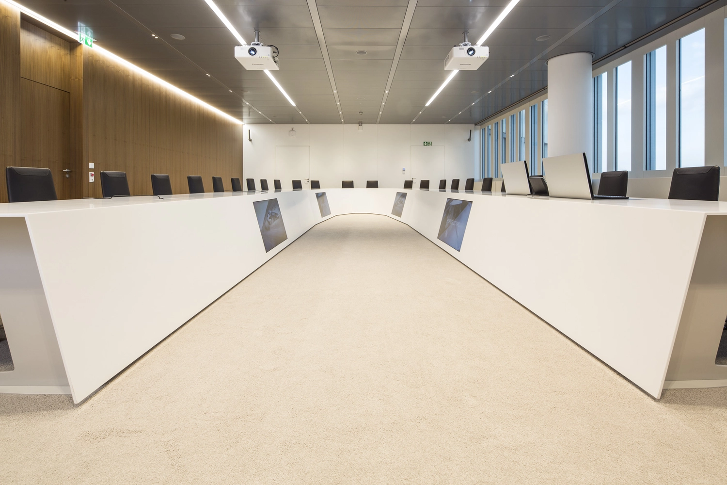EMshield GmbH – Architektur und Unternehmenssicherheit – Dieses Bild zeigt einen modernen Konferenzraum mit einem großen, U-förmigen Konferenztisch von Holzmedia mit integrierter Technologie.